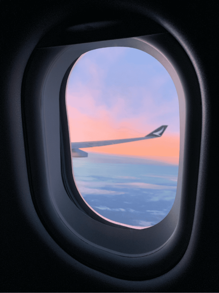 Aircraft wing and pink sunrise sky seen through a plane window