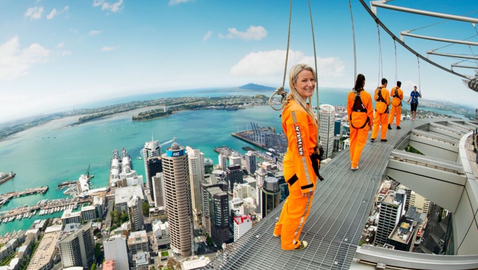 A SkyWalk participant in an orange suit on the Sky Tower's outdoor walkway above Auckland