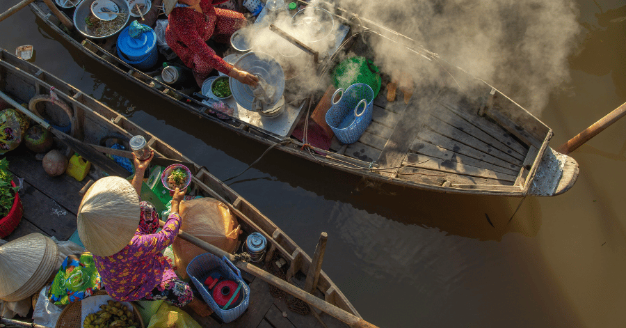 Traders in conical hats selling from wooden boats at a misty Mekong Delta floating market