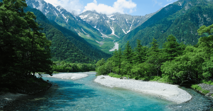 Clear turquoise river winding through a green valley below the snow-capped Japanese Alps