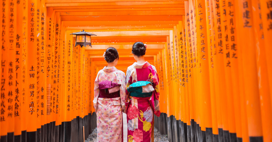 Two women in kimono walking through the red torii gates at Fushimi Inari Shrine, Kyoto