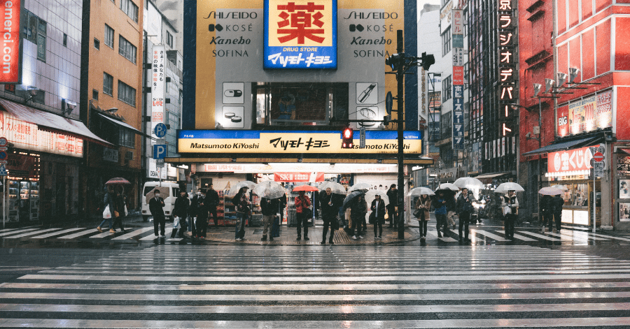 People with umbrellas crossing a wet Japanese shopping street on a rainy day