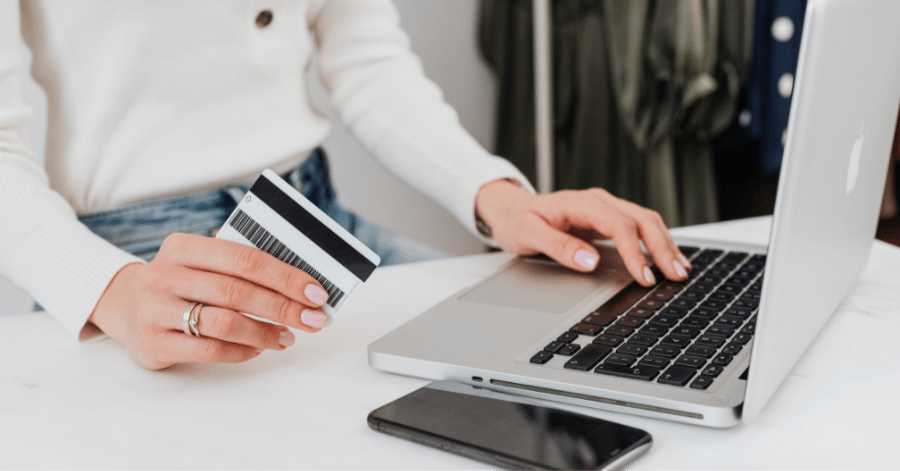 Person holding a credit card while typing on a laptop, smartphone beside them