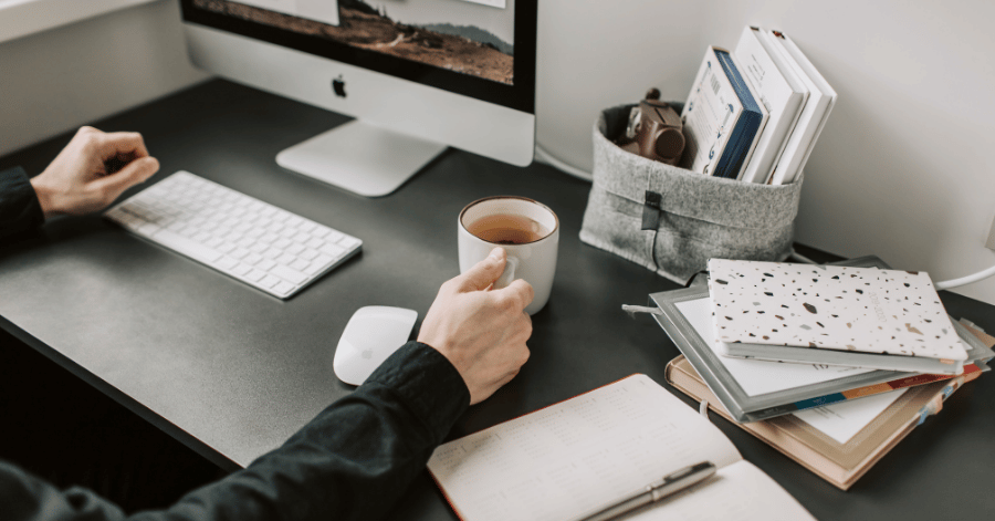 Person working at a tidy desk with an iMac, keyboard and a cup of coffee