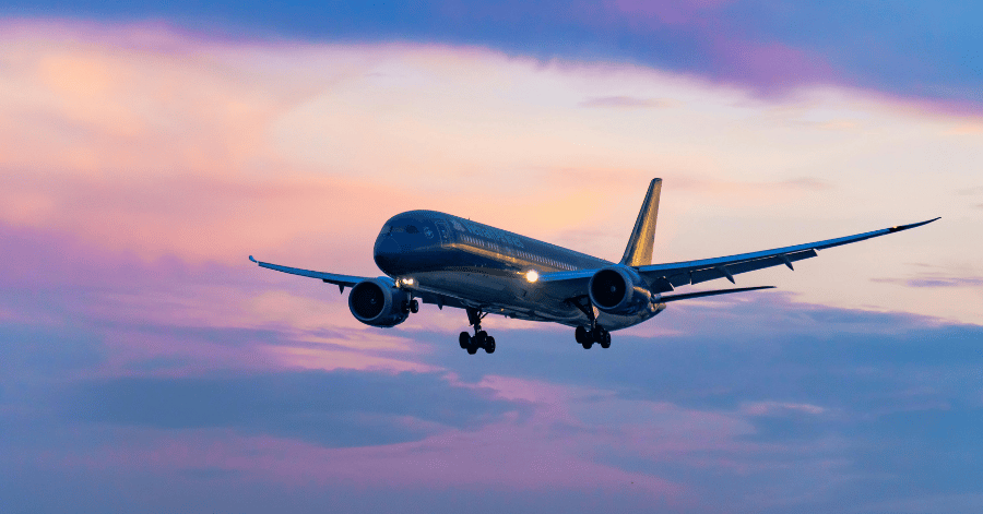 A passenger jet with its landing gear down flying against a pink and purple sunset sky