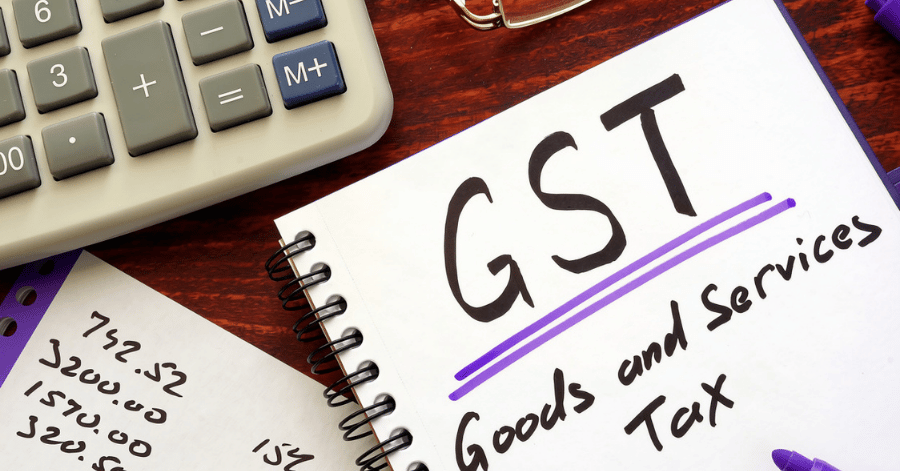 A spiral notebook reading 'GST Goods and Services Tax' beside a calculator and handwritten sums on a desk
