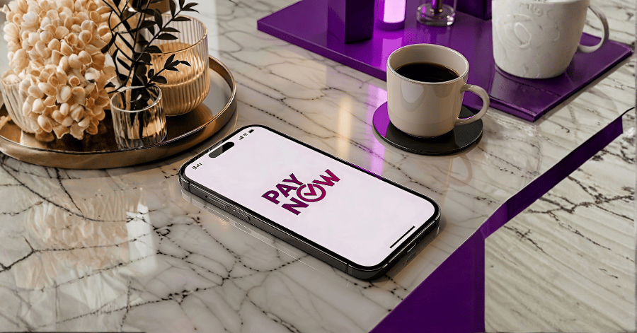 Smartphone displaying the PayNow logo, resting on a marble table beside a cup of coffee