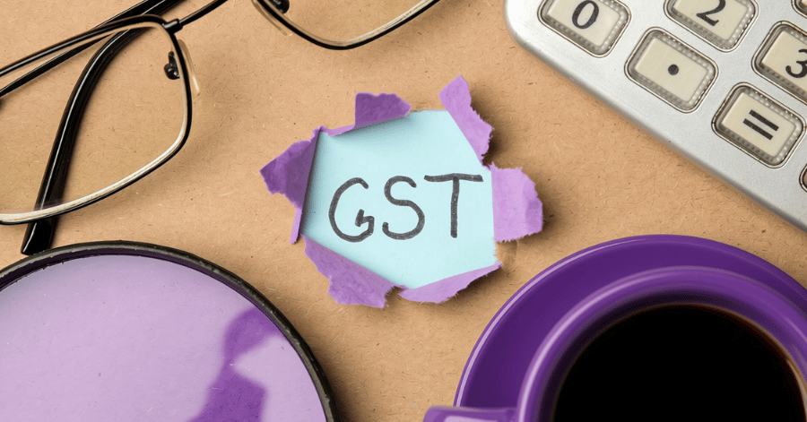 Handwritten GST note torn through purple paper on a desk with glasses, a calculator, and a cup of coffee