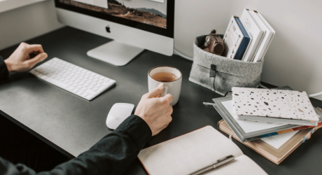 Person working at a tidy desk with an iMac, keyboard and a cup of coffee