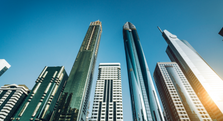 Low-angle view of modern glass-tower skyscrapers in a business district against a clear blue sky