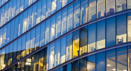 Curved glass facade of a modern corporate office building lit up at dusk
