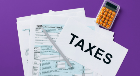 Tax return forms and a sheet reading TAXES beside an orange calculator on a purple background
