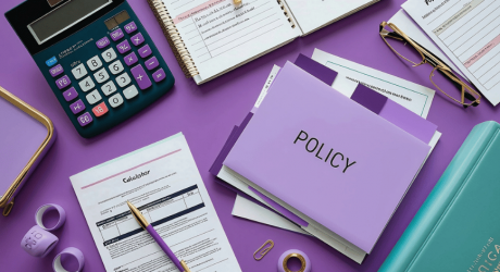 Purple folder labelled 'Policy' beside a calculator, business forms, a notebook and glasses on a desk