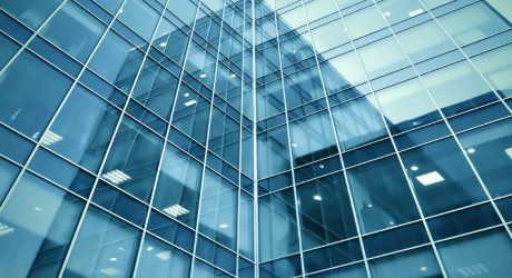 Low-angle view of a blue glass office tower with reflections across its windows