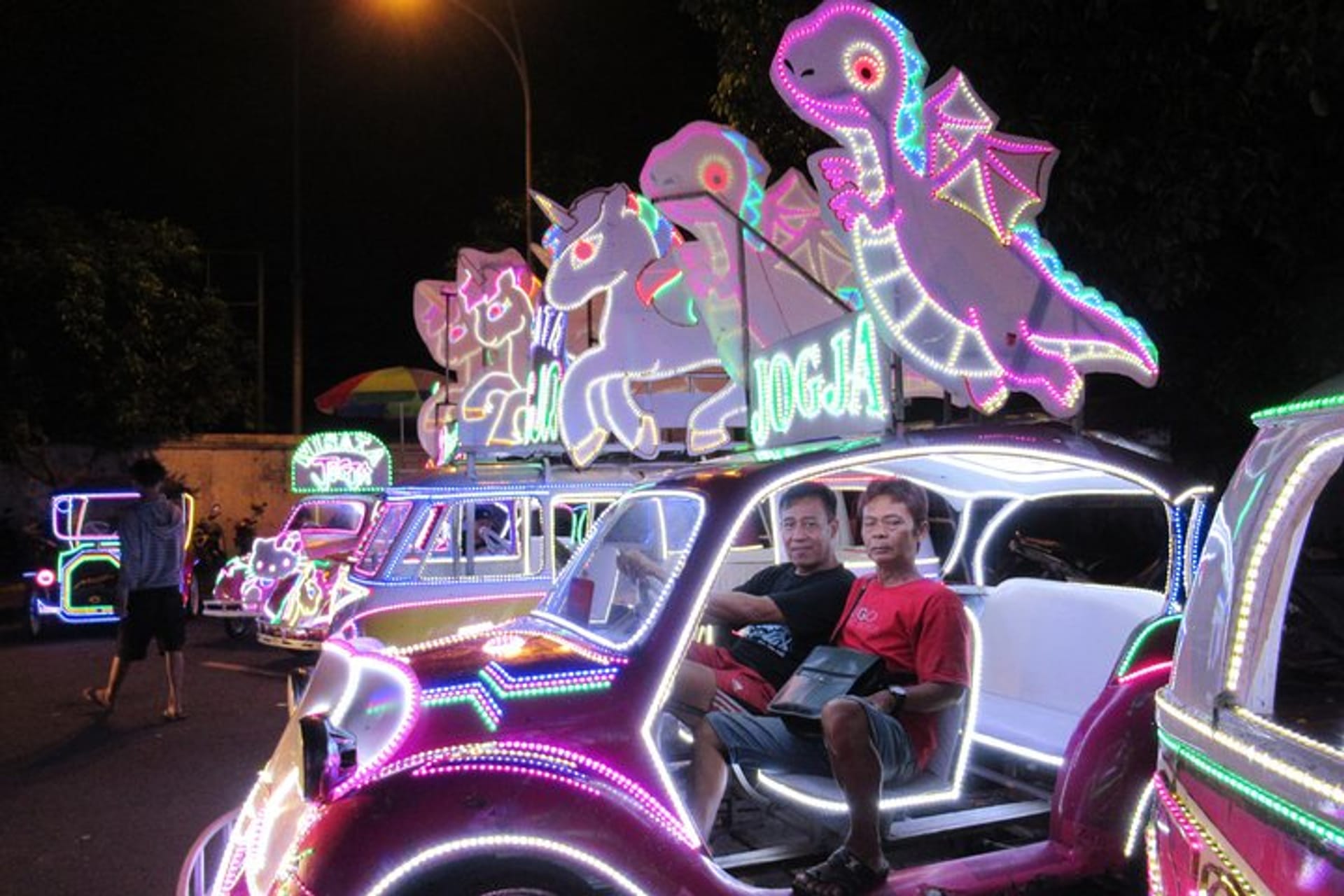 Neon-lit pedal cars glowing with unicorn and dragon lights at Alun-Alun Kidul after dark