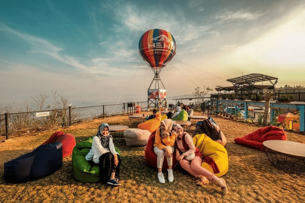 Visitors on beanbags at HeHa Sky View's hilltop terrace beside its balloon sculpture at sunset