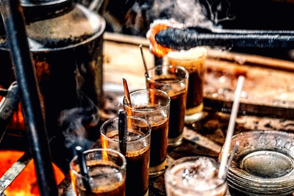 Glasses of kopi joss, charcoal-infused coffee, beside glowing embers at a street stall