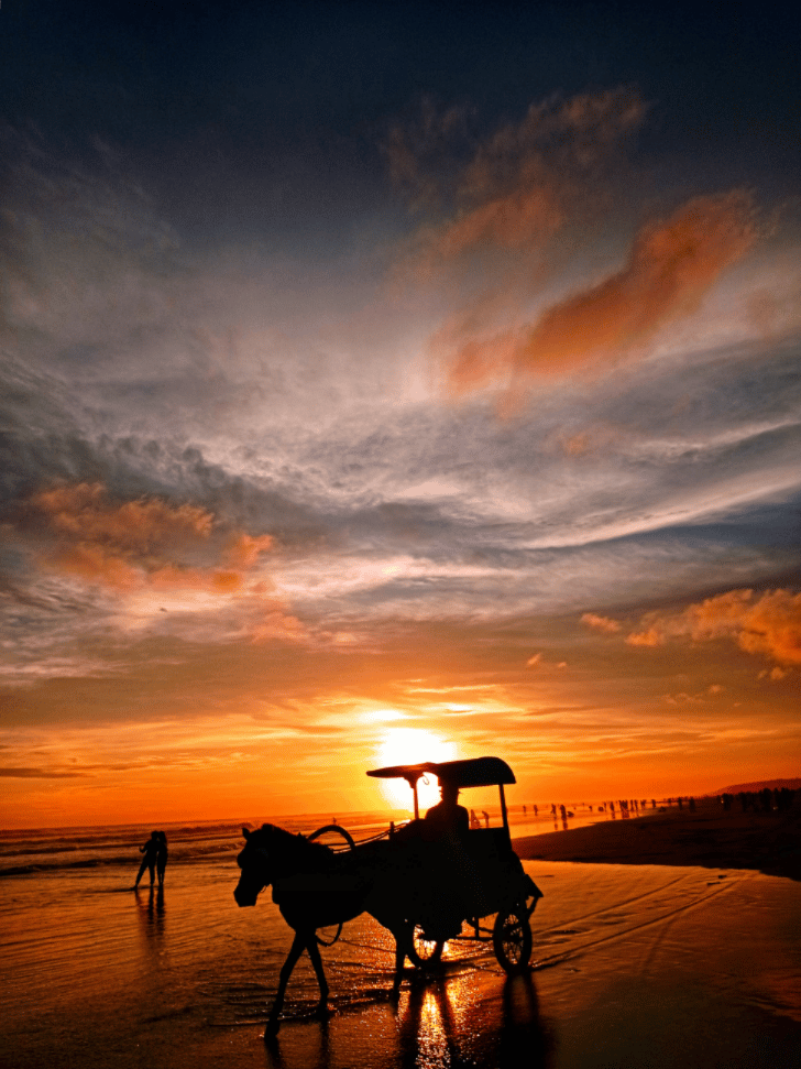 A horse-drawn andong carriage silhouetted on a Yogyakarta beach at sunset