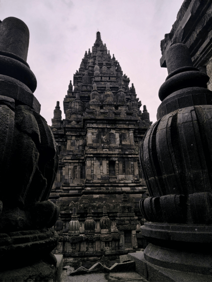 A Prambanan temple spire framed between dark, carved stone pillars