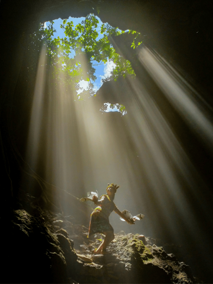 A shaft of sunlight streams into Jomblang Cave, lighting a visitor on the rocks below
