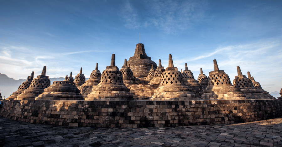 Rows of bell-shaped perforated stupas on Borobudur's upper terrace against a blue sky