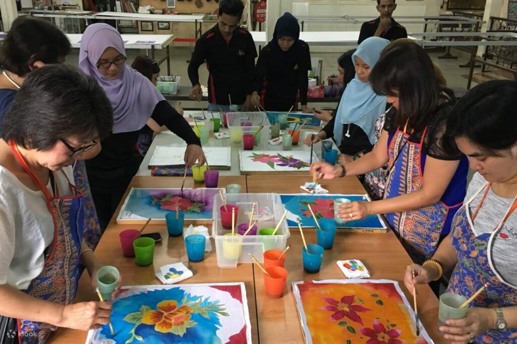 Participants painting colourful floral batik with brushes at a Kuala Lumpur workshop