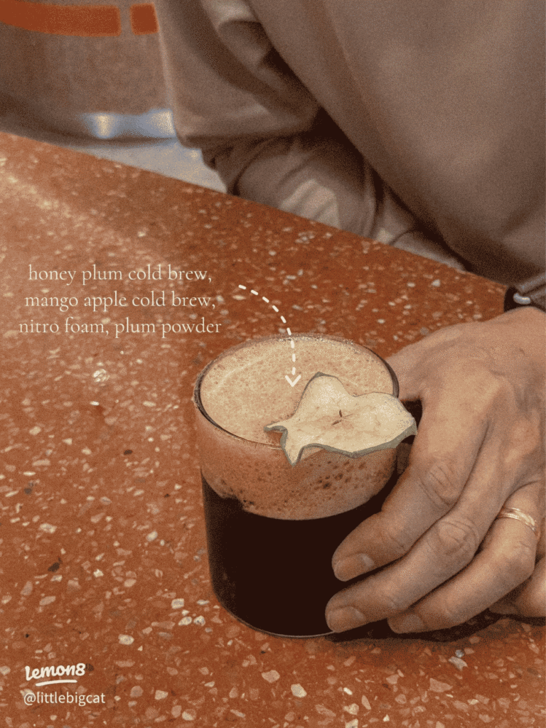 A hand holding a glass of honey plum cold brew at 103 Coffee