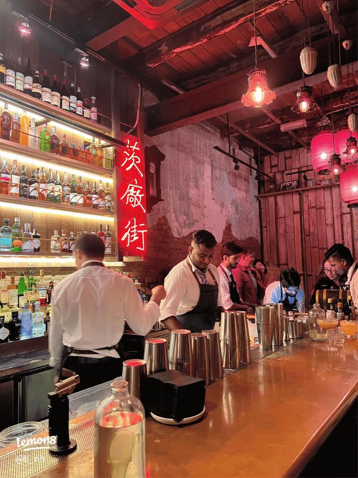 Bartenders mixing drinks behind the bar at PS150, a dim speakeasy with red Chinese signage
