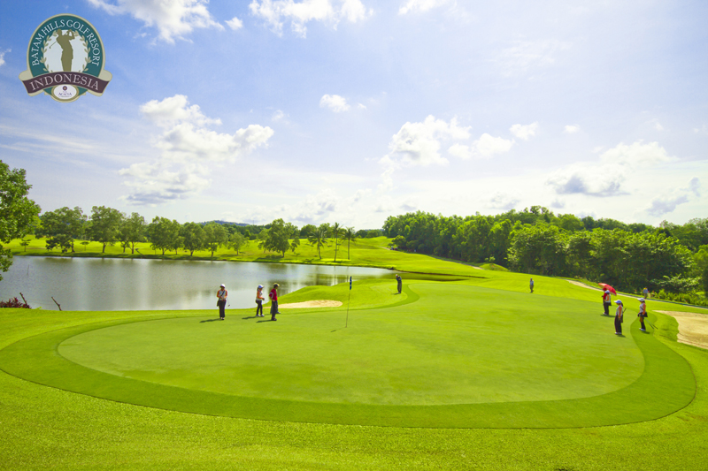 Golfers putting on a green beside a lake at a Batam golf resort