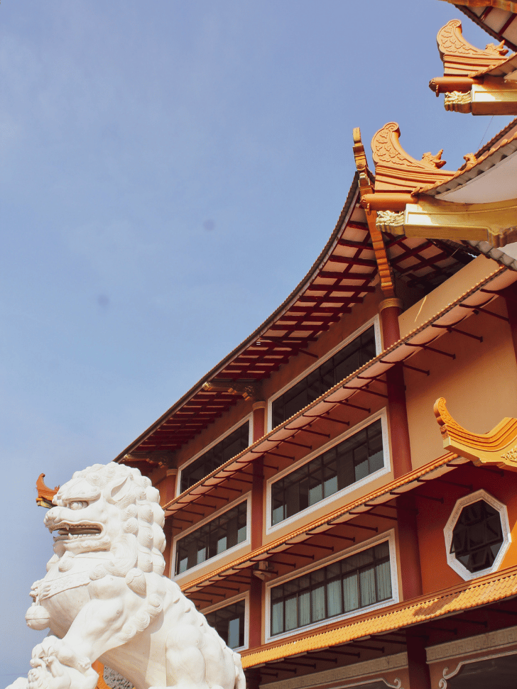 A stone lion and gold-tipped roof at Maha Vihara Duta Maitreya Temple, Batam