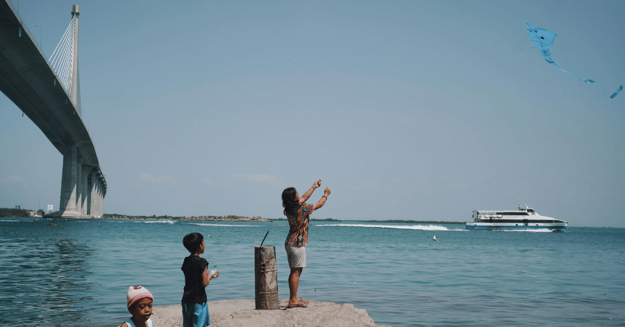 A family flies a kite beside Barelang Bridge as a ferry speeds past, Batam
