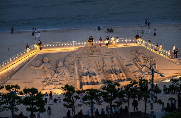 Large illuminated sand sculptures on Haeundae Beach at dusk during Busan's summer Sand Festival