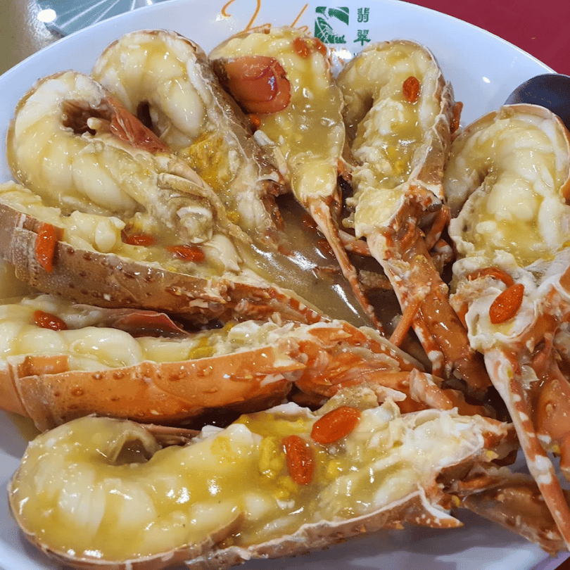 Lobster halves in golden broth scattered with goji berries on a white plate