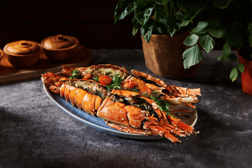 Grilled lobster halves topped with herbs and tomato on a platter, styled on a dark table
