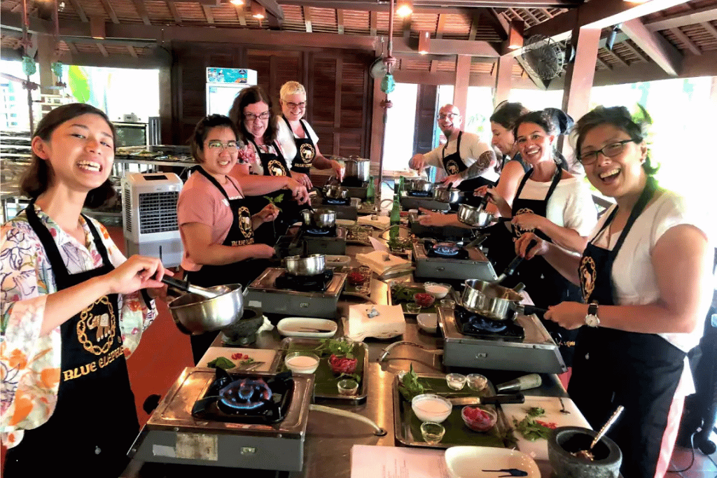 Smiling participants in aprons at cooking stations during a Blue Elephant Thai cooking class