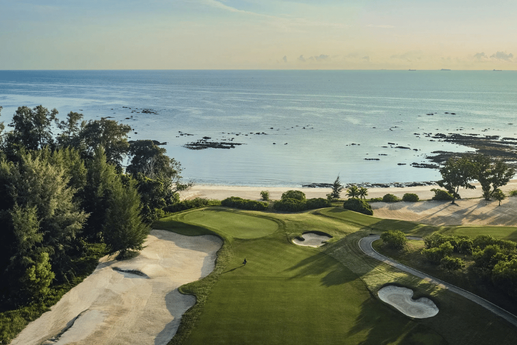 Aerial view of a green fairway and sand bunkers running down to the sea at The Els Club Desaru Coast