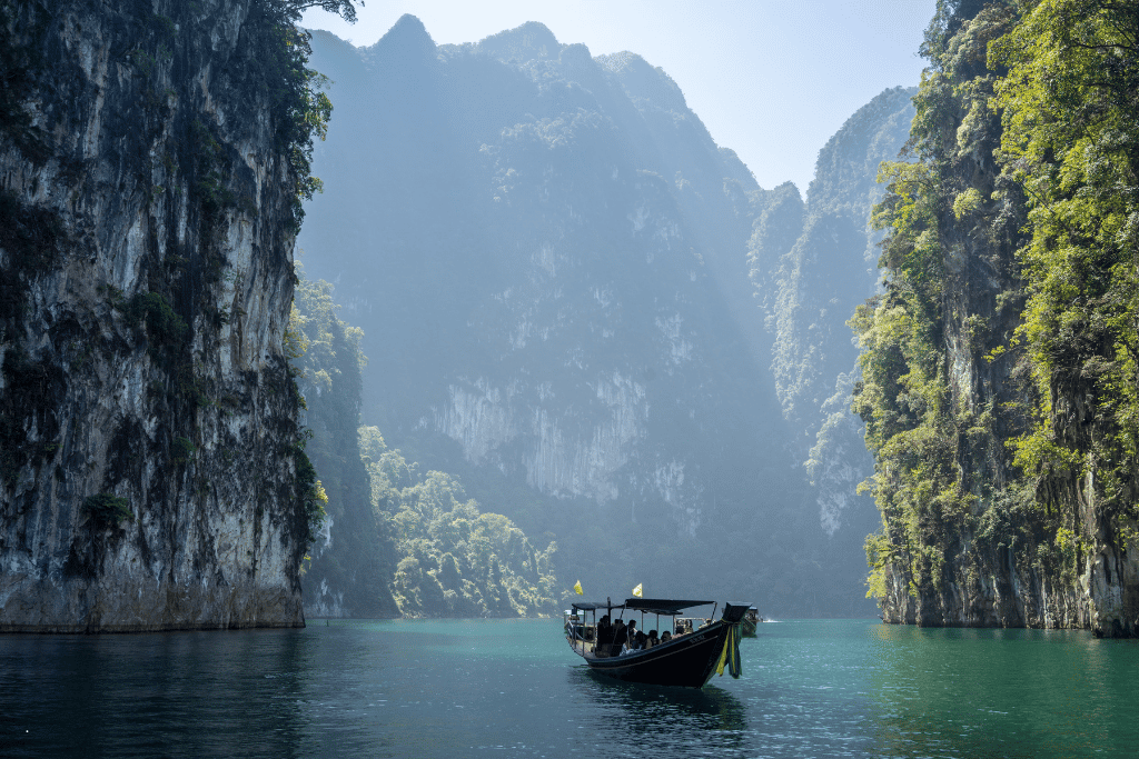 A tour boat dwarfed by towering jungle-covered limestone cliffs on calm green water