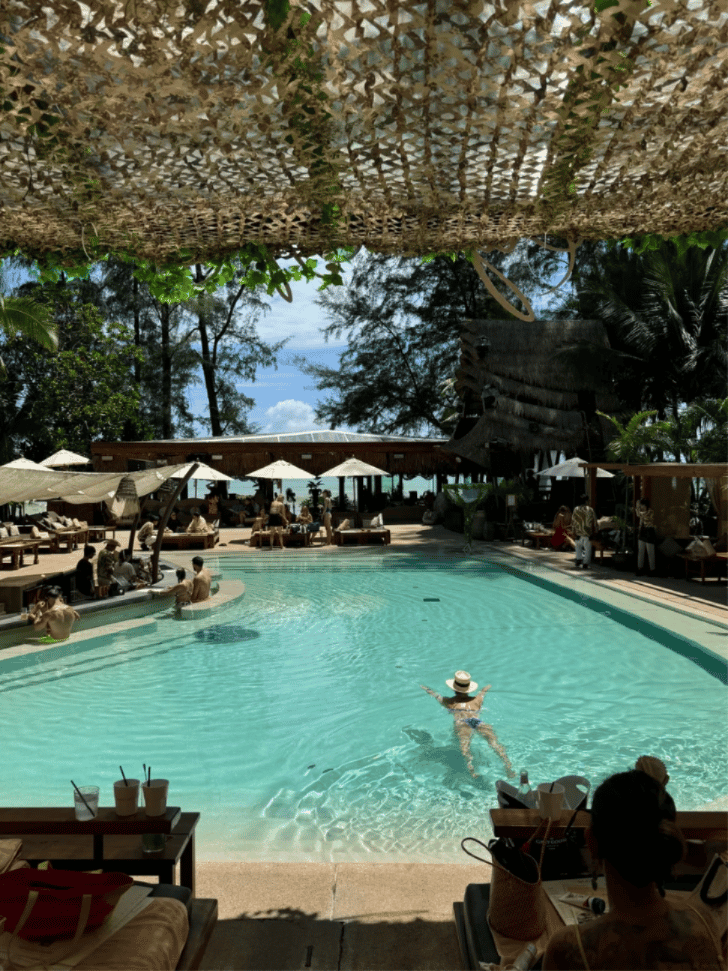 Pool, day beds and camouflage-net shade at a Kamala Beach beach club overlooking the sea