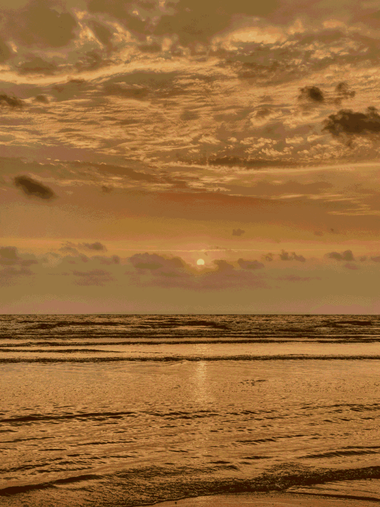 Sun low over the sea at Desaru with an orange sky reflected on wet sand