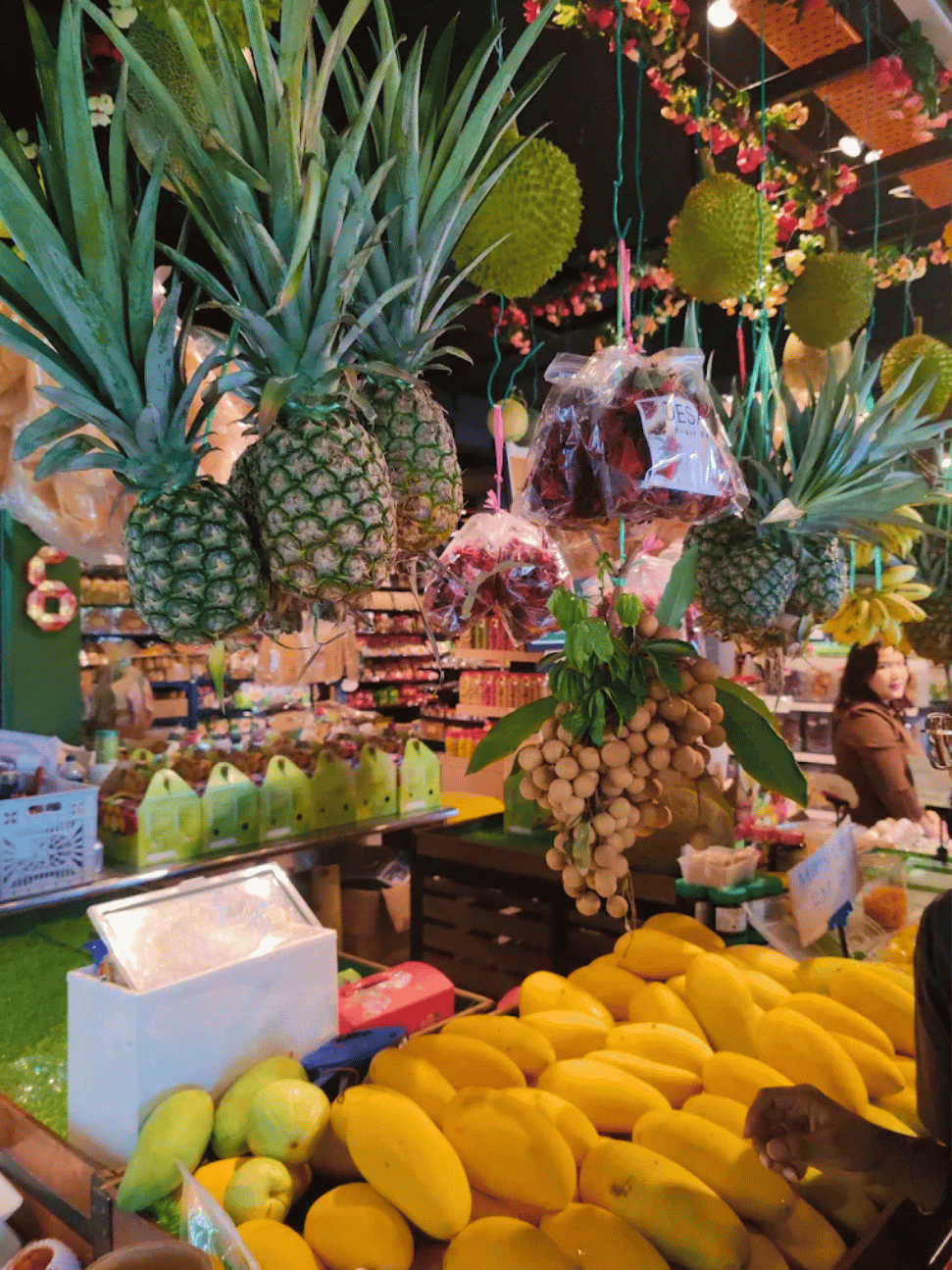 Pineapples, durians and longans hanging above a counter piled with mangoes at Desaru Fruit Farm