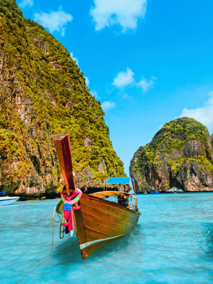 Wooden longtail boat moored below the towering limestone cliffs of Maya Bay on a clear day