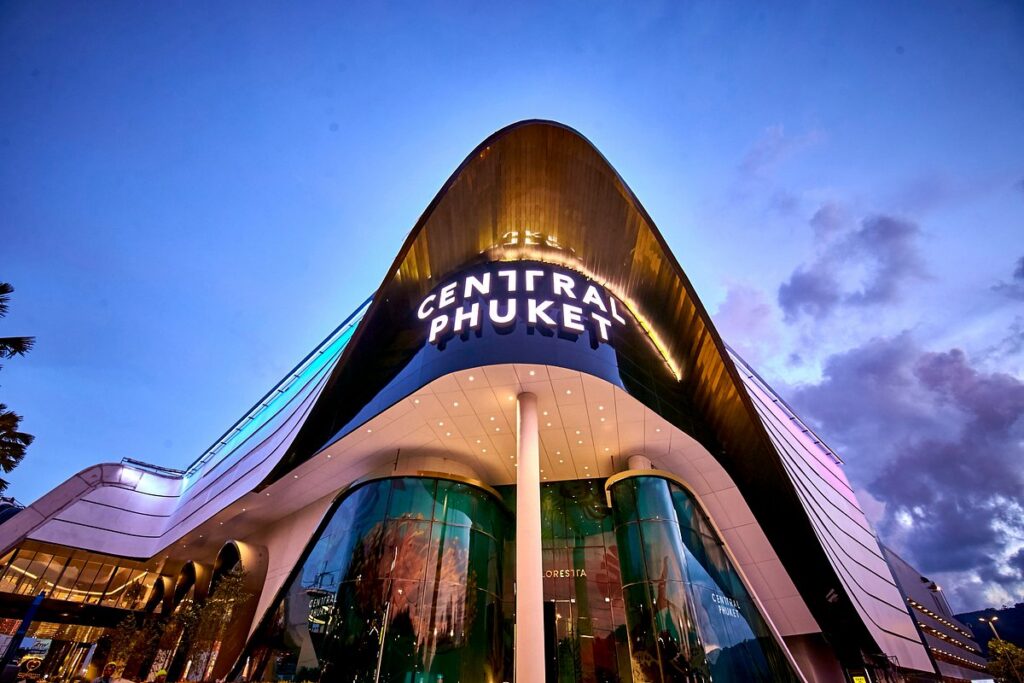 The illuminated curved facade and glass entrance of Central Phuket mall at dusk