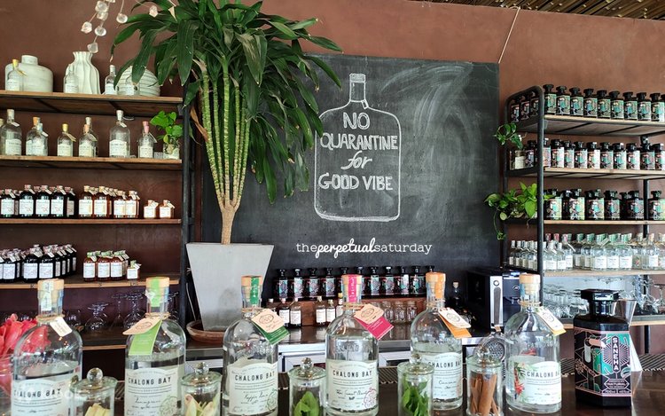 Rows of Chalong Bay rum bottles on shelves beside a chalkboard sign in the distillery