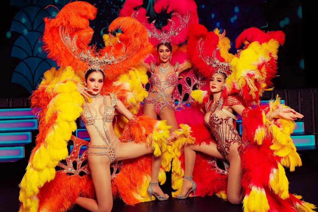 Three performers in elaborate feathered showgirl costumes on stage at Simon Cabaret