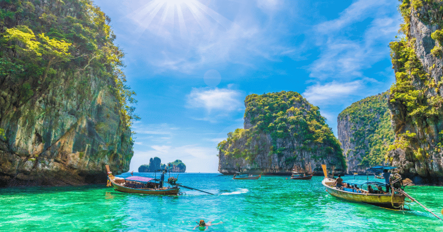 Longtail boats and a snorkeller among limestone islets in the clear sea off Phi Phi