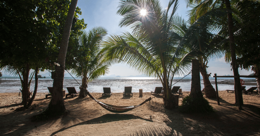 A hammock strung between palm trees on a quiet Koh Yao beach at golden hour