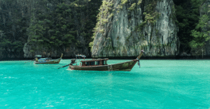 Two wooden longtail boats on turquoise water below a green limestone cliff near Phi Phi