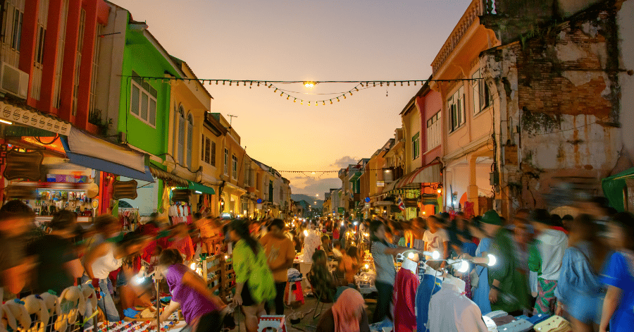 Crowds and string lights along a Phuket Old Town street market at dusk