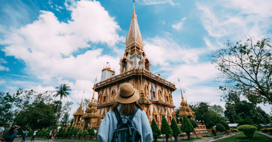A traveller in a straw hat looking up at the ornate Grand Pagoda of Wat Chalong