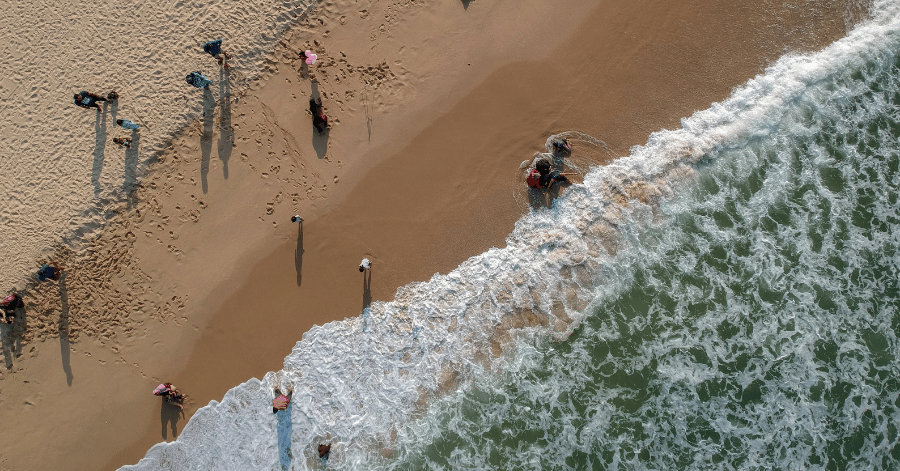 Aerial view of beachgoers on Desaru's sand as surf breaks along the shoreline